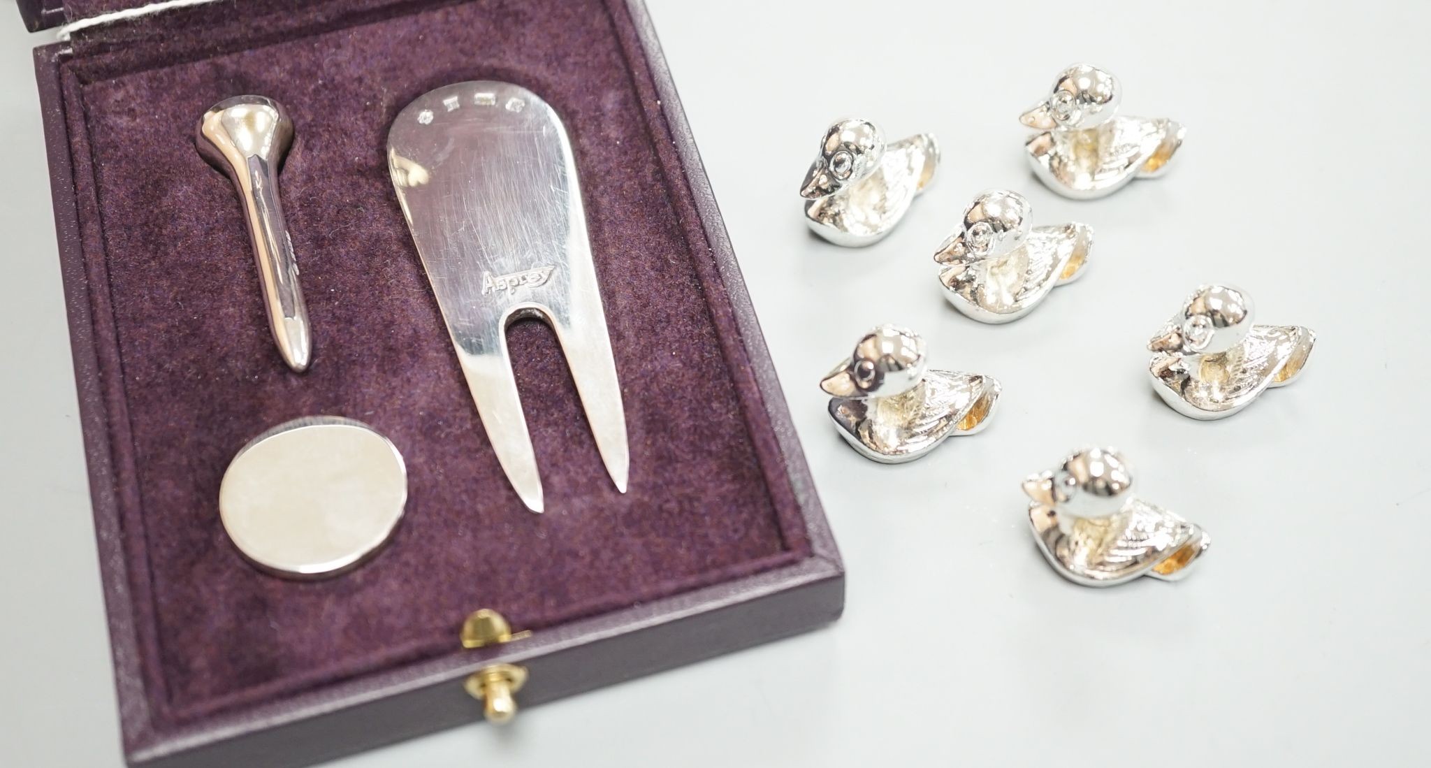 A modern Asprey cased silver golfer's companion set, comprising a tee, marker and pitch mark repairer, together with a set of six metal duck menu holders.